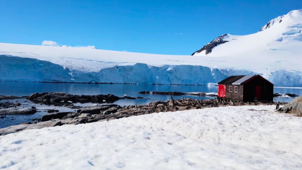 A full shot of Port Lockroy, framed by snowy mountains, depicting an Antarctic expedition scene.