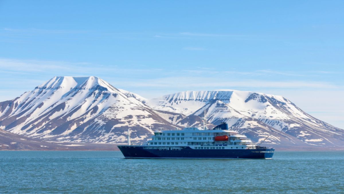 An Antarctic expedition cruise ship navigates through water, surrounded by majestic mountains.
