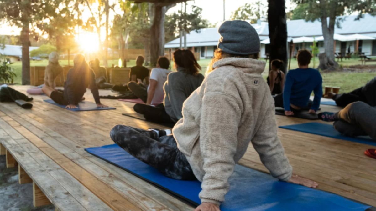 A group of individuals participating in an outdoor yoga session during a corporate event retreat, with the sun setting in the background.