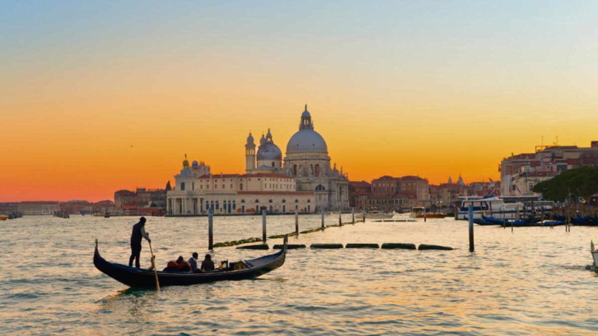 Gondola gliding through water at sunset, with a stunning view of Venice's skyline in the background.