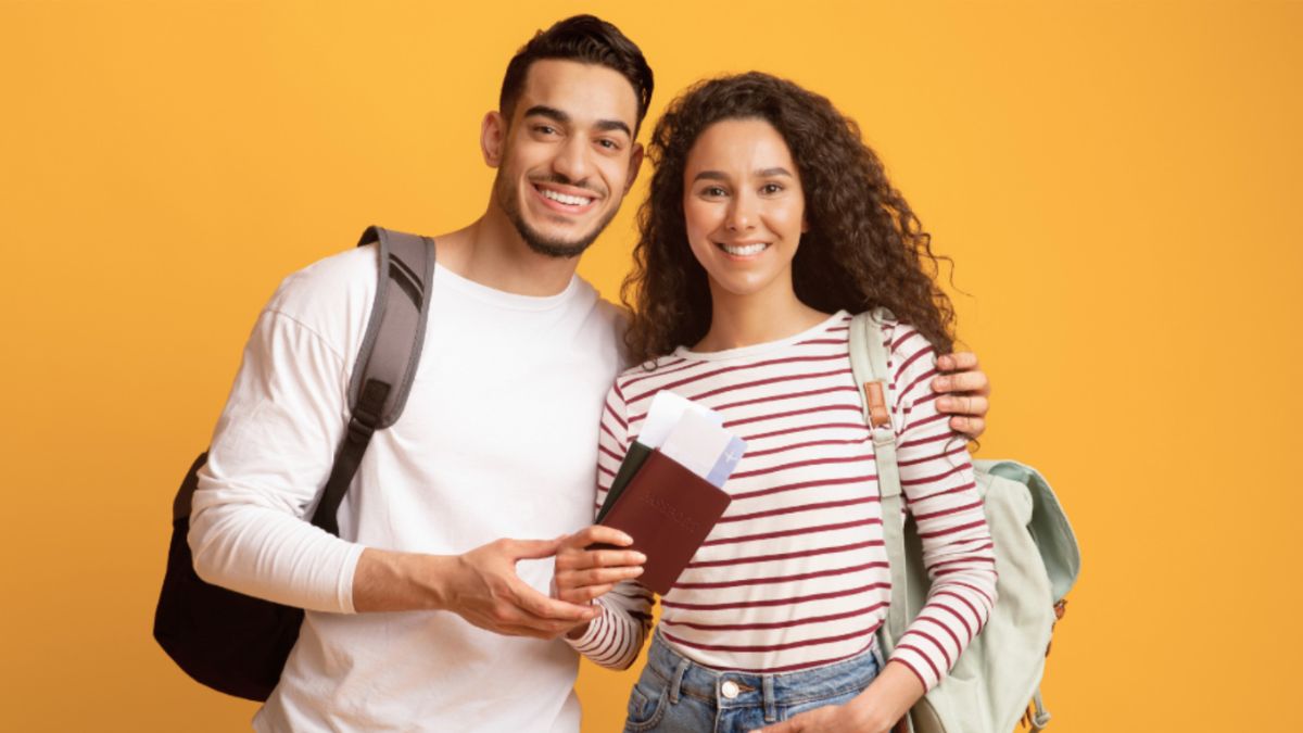 A young couple excitedly holds a passport and a backpack, preparing for their ocean cruise adventure.