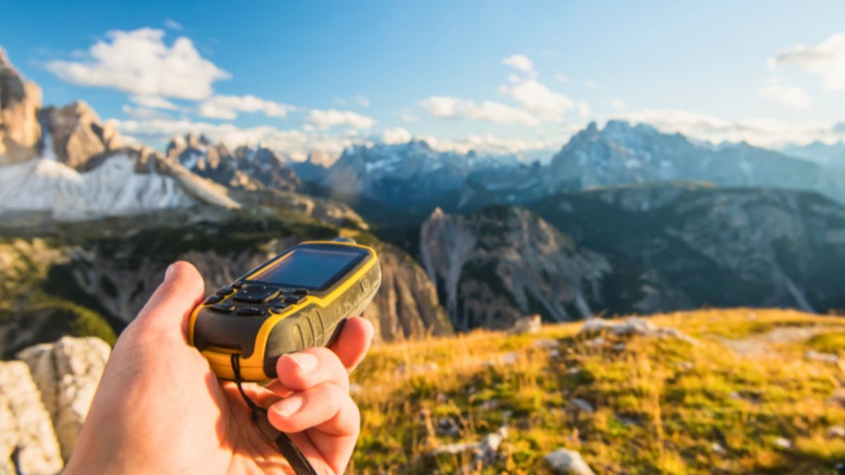 A hand holds a GPS device while navigating through rugged mountain terrain during an expedition travel adventure.