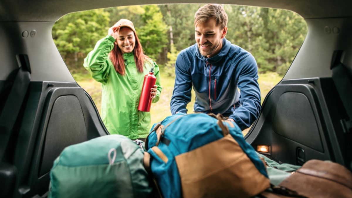 A man and woman pack bags into the trunk of a car, preparing for an expedition travel adventure.