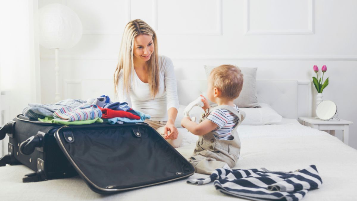 A woman and a baby sit on a bed surrounded by luggage, planning for an upcoming ocean travel adventure.