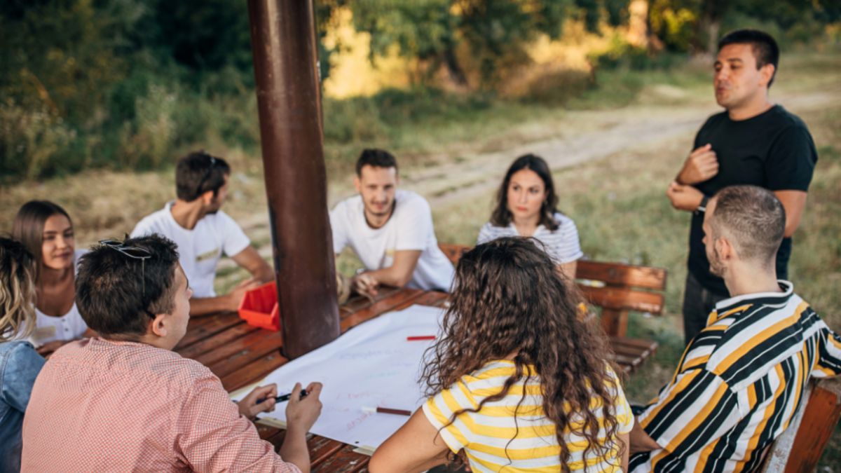 Corporate Event Retreats Abroad:<br>Top 10 International Destinations 3 A group of professionals gathered around a picnic table during a corporate retreat, engaged in conversation and collaboration.