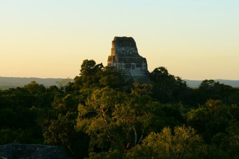 A large Maya stone structure sitting atop a lush green Guatemalan jungle
