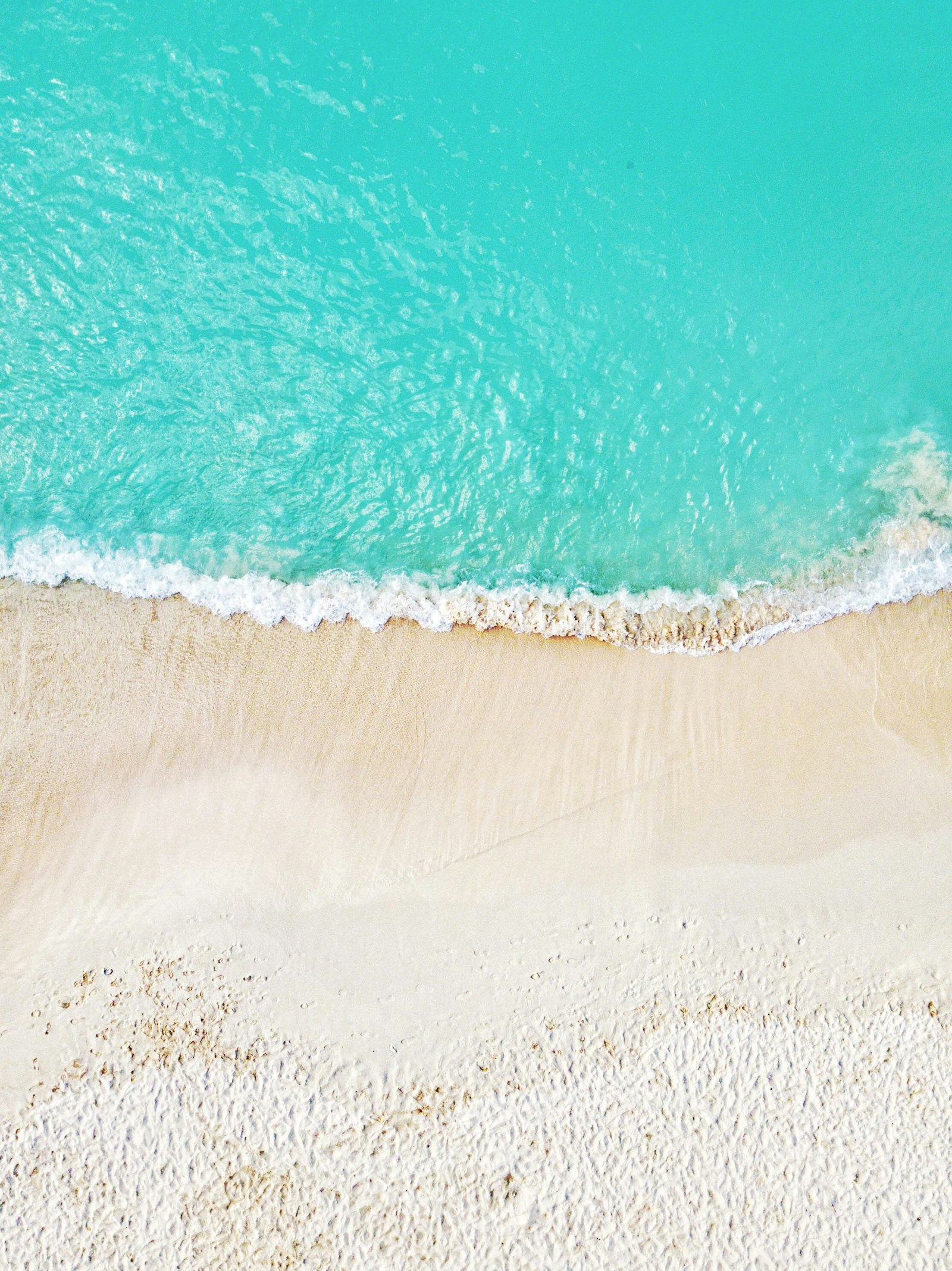 Aerial view of a curving white sand coastline meeting clear blue water