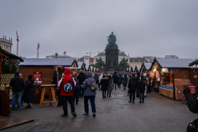 Crowded European Christmas market with wooden stalls, lights and a historic statue
