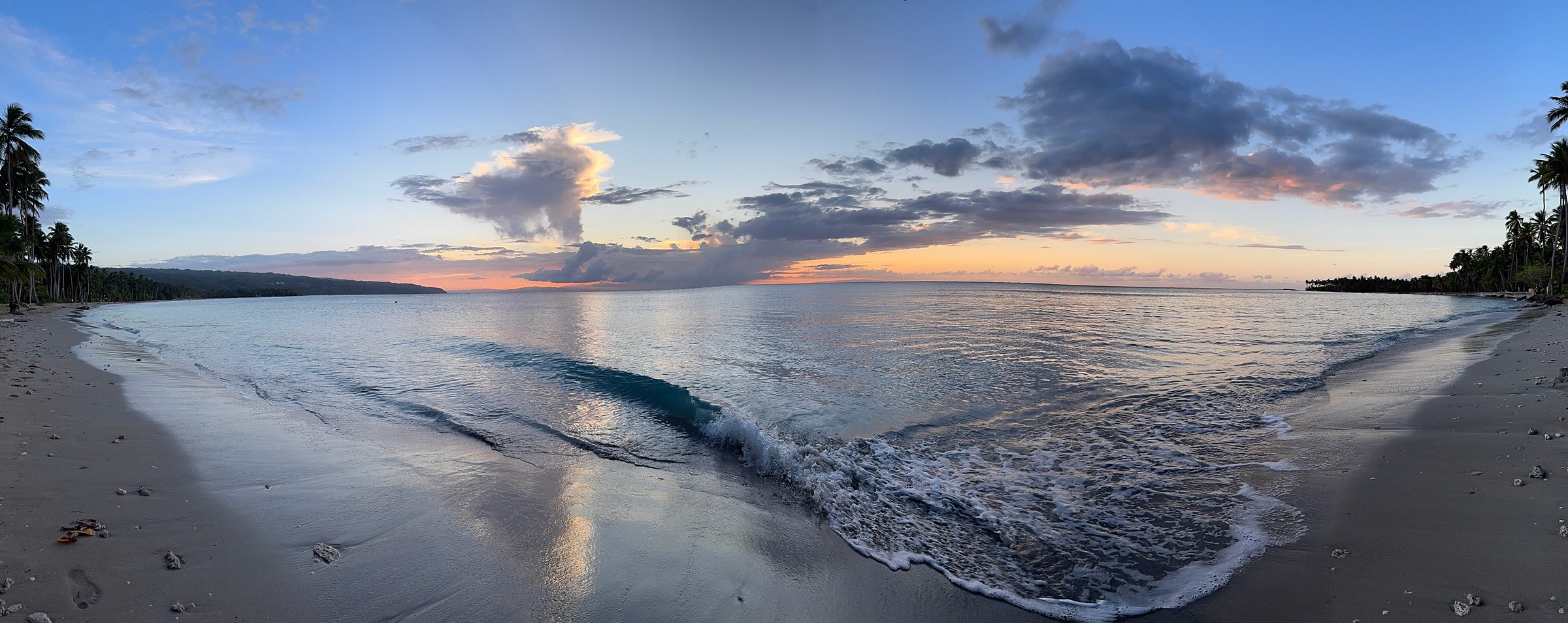 Sunset over a palm-fringed Caribbean beach with waves washing the shore