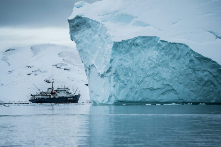 Small expedition boat navigating beside a towering Arctic iceberg in Greenland