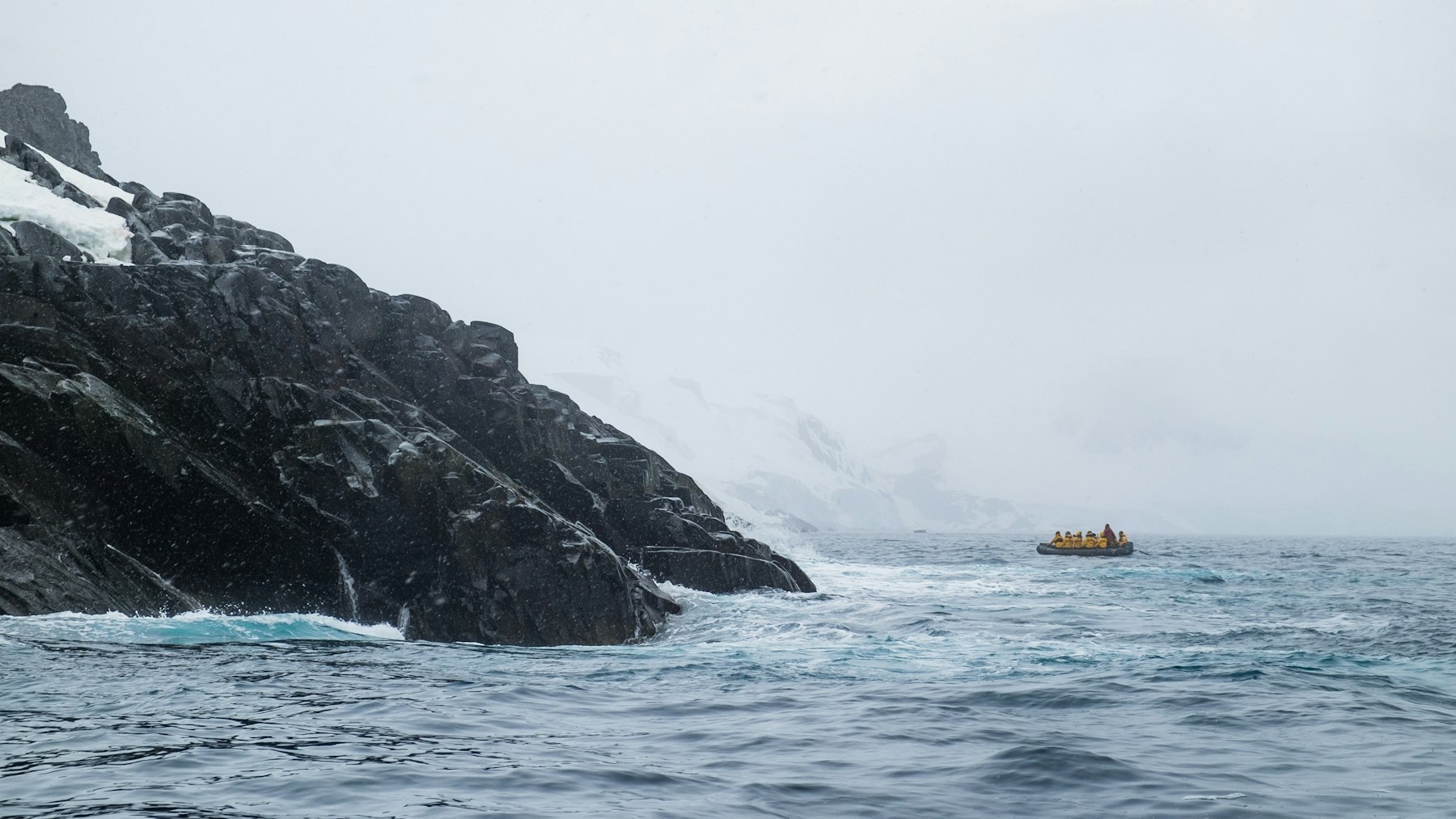 A Zodiac carrying passengers along a rocky shore during an Antarctica expedition cruise landing