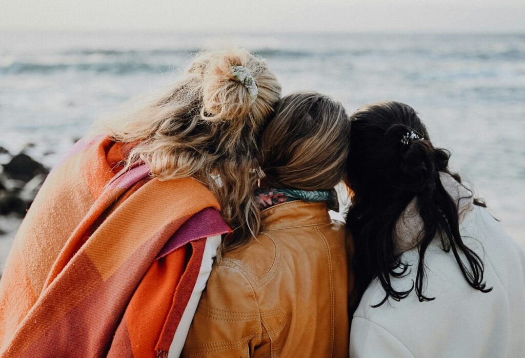 The best girls trip destinations start with the group: three friends sitting together looking out over the ocean.