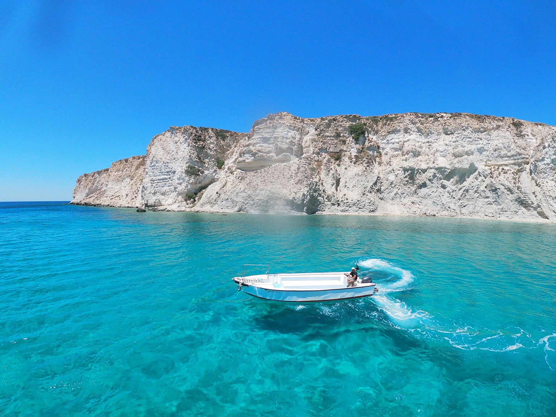 A blue and white boat on calm water below the rocky coast of Crete, one of the best Greek islands to visit for World Heritage sites
