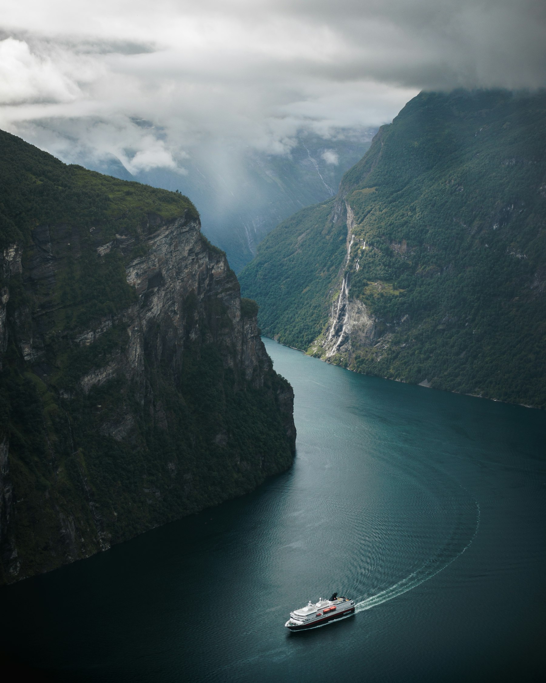 A small boat crossing Geirangerfjord beneath sheer mountain walls in Norway, among the best places to visit in Europe in high summer