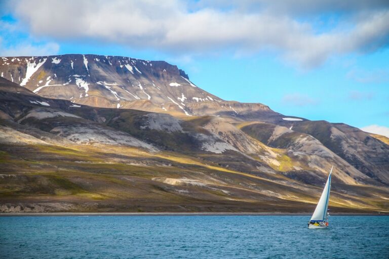 Expedition sailboat beneath snow-covered mountains in Svalbard, Arctic Norway