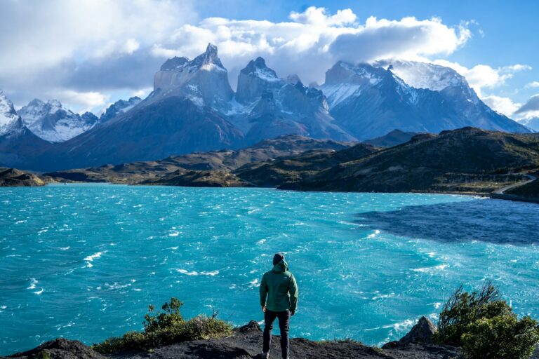 A hiker standing above a lake below the granite peaks of Torres del Paine in Chile, the classic image of hiking Patagonia.