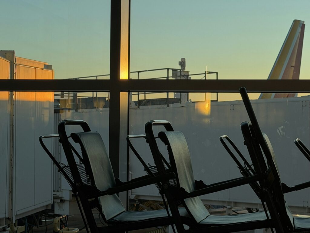 Empty departure gate seating silhouetted against a terminal window at dusk, the kind of gate where airline elite status is quietly spent