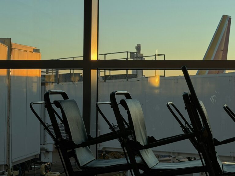 Empty departure gate seating silhouetted against a terminal window at dusk, the kind of gate where airline elite status is quietly spent