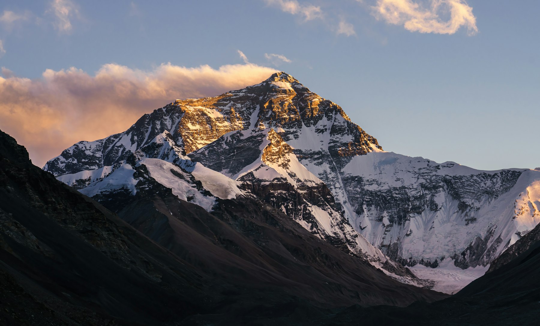 Snow and rock on the summit of Mount Everest catching sunrise light above dark Himalayan ridges