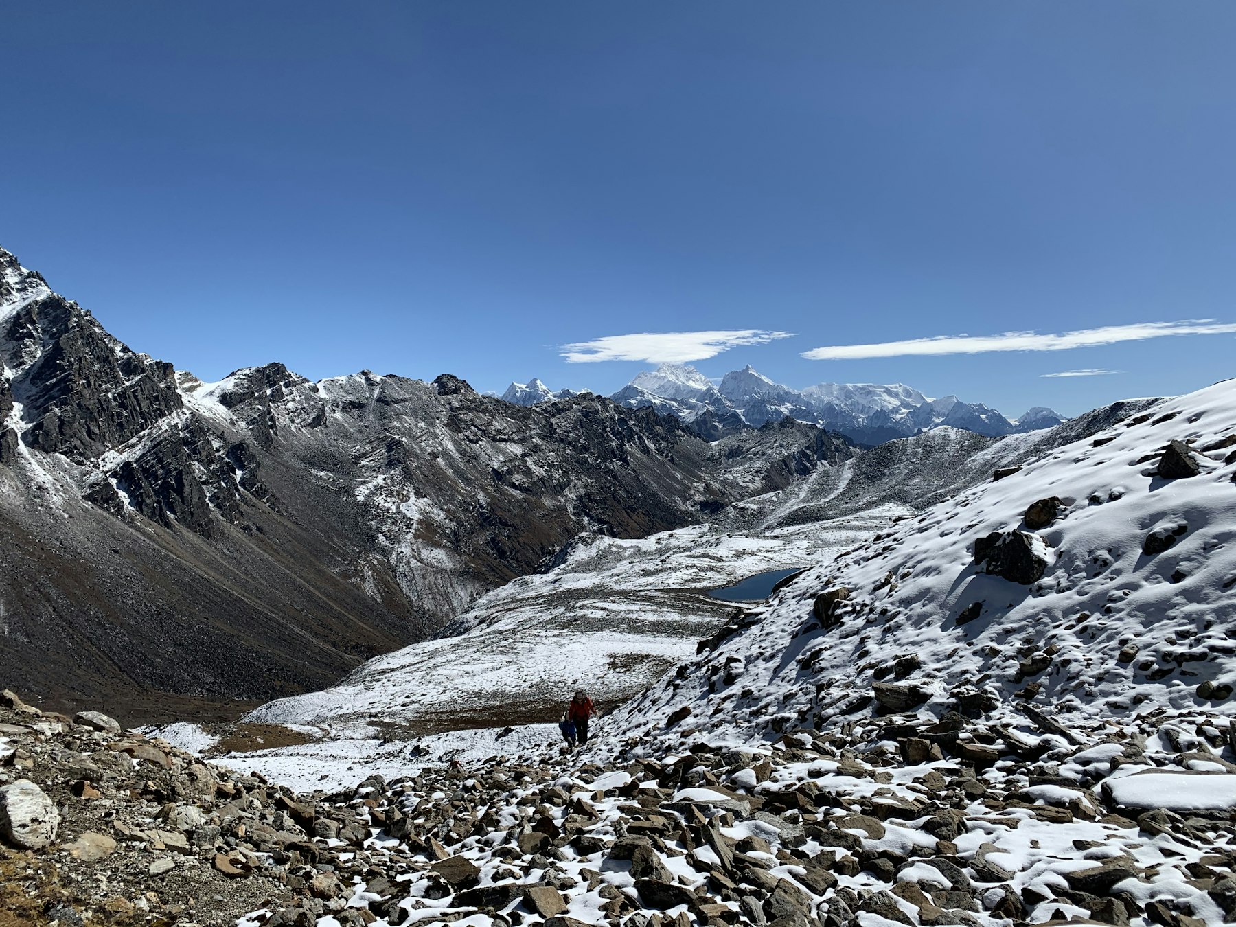 A lone trekker crossing a snow-covered scree slope above a glacial valley in the Nepali Himalaya