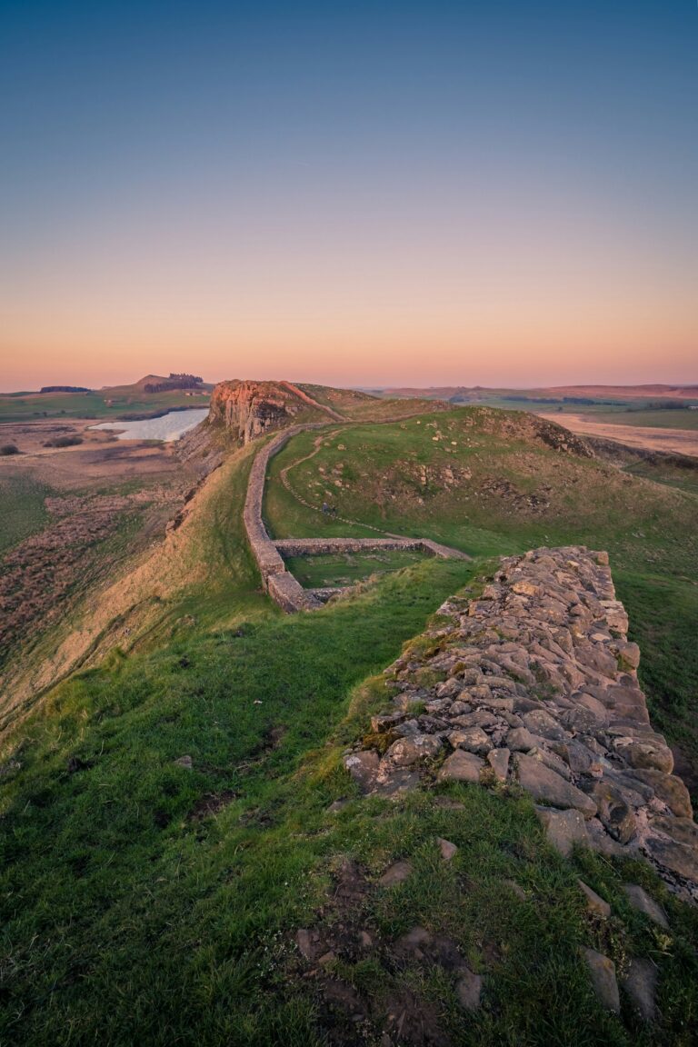 Hadrian's Wall running along a crag ridge in Northumberland at first light, the line of the Roman frontier receding to the horizon.