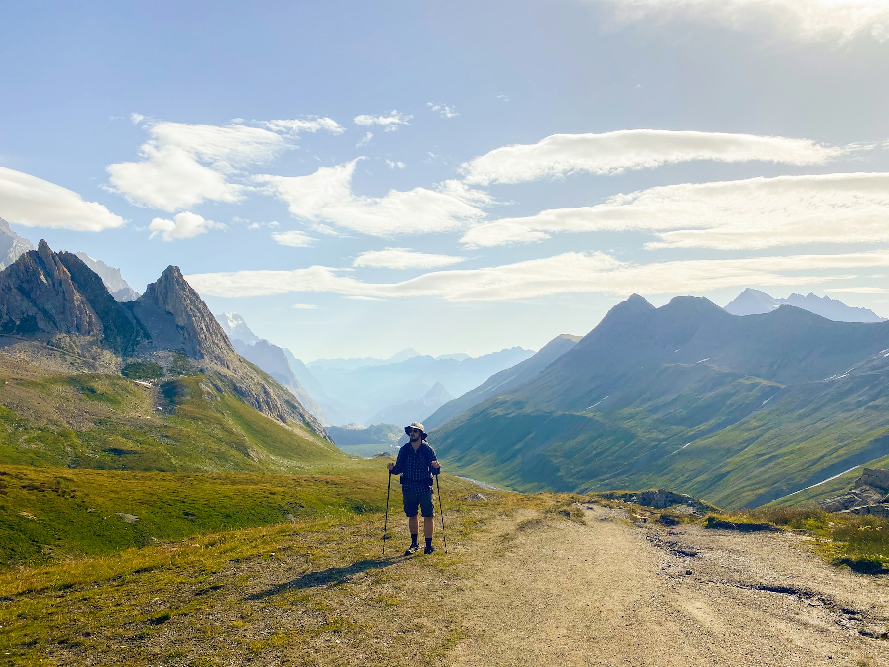 A walker on the Tour du Mont Blanc descending from the Col de la Seigne into a wide green valley