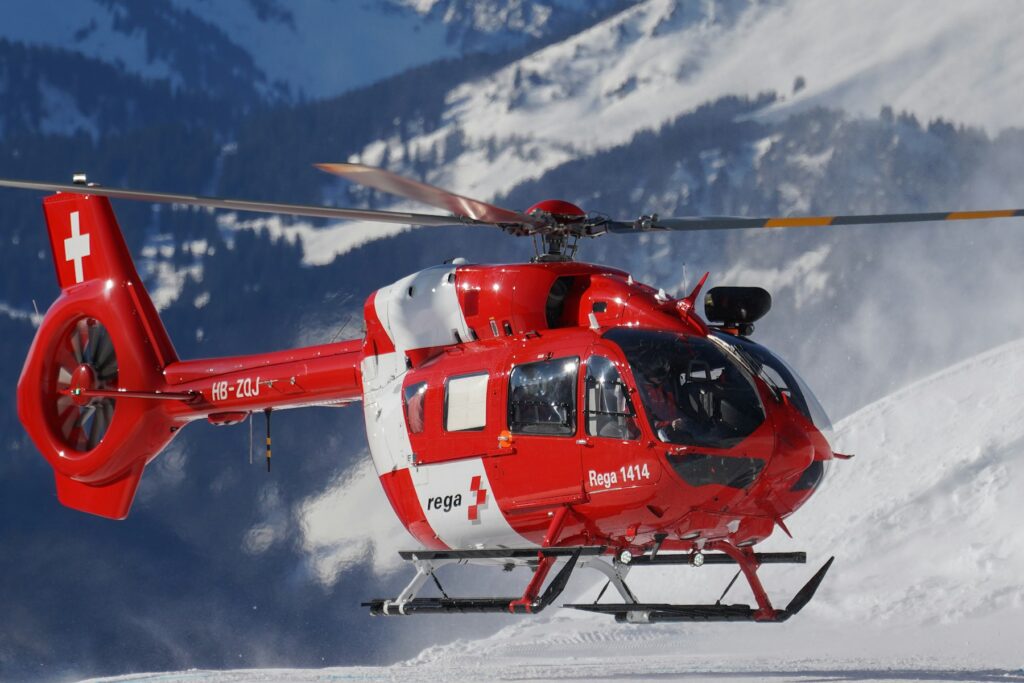 A mountain rescue helicopter hovering above a snow slope in Switzerland, the kind of evacuation travel insurance is bought to pay for.