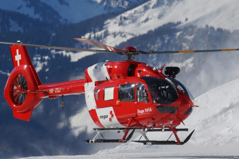 A mountain rescue helicopter hovering above a snow slope in Switzerland, the kind of evacuation travel insurance is bought to pay for.