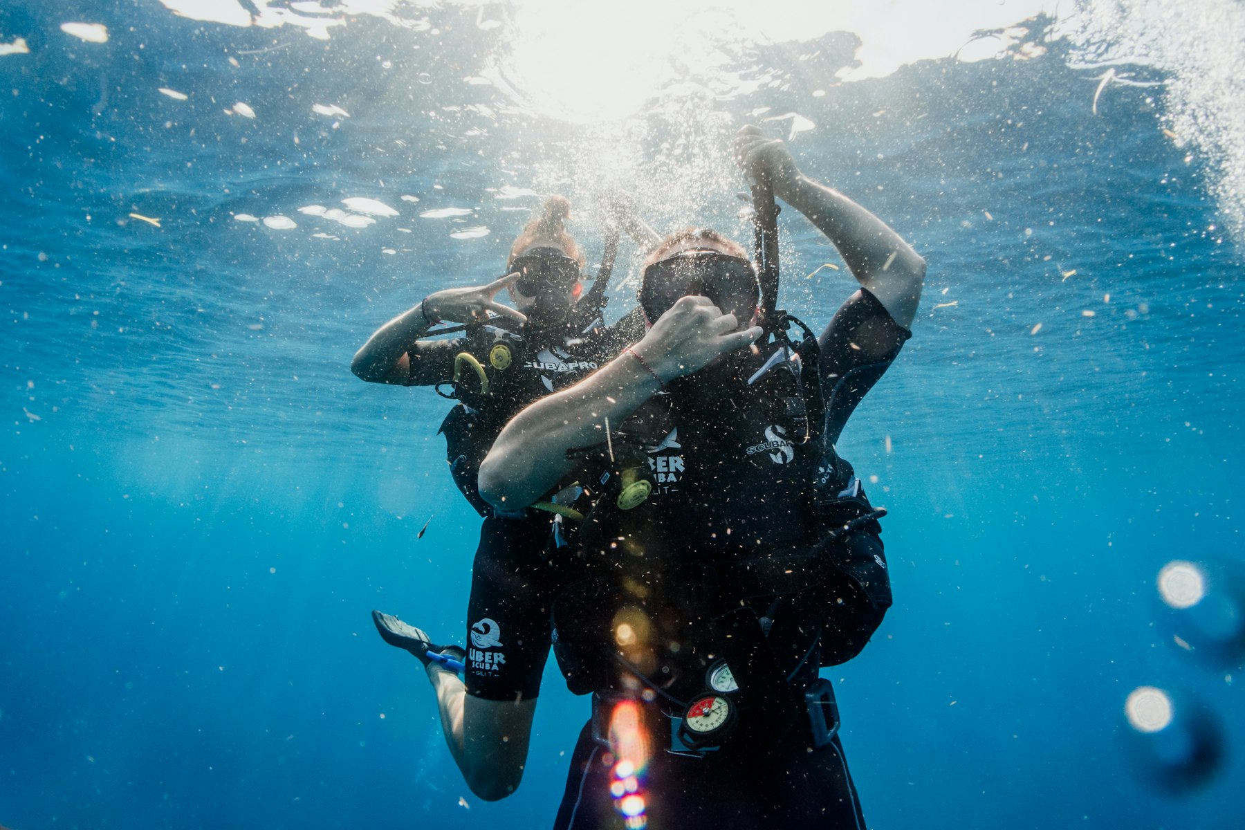 Two scuba divers descending through blue water in Indonesia, the kind of activity a travel insurance policy may exclude by default.